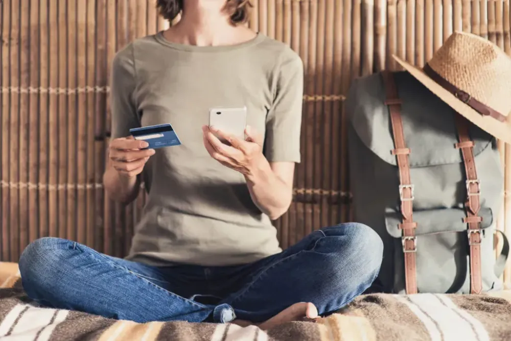 Woman holding a smartphone and credit card next to her packed backpack